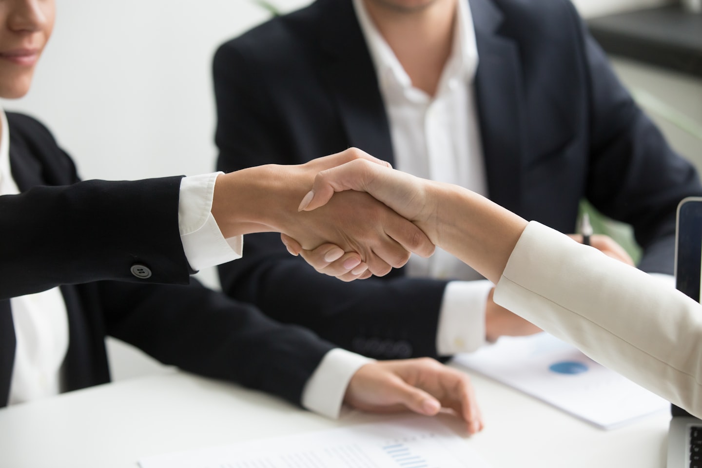Dos profesionales de negocios se dan la mano sobre un escritorio en una oficina.